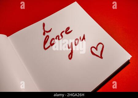 Eine Liebeserklärung ist in Lippenstift auf Papier auf rotem Hintergrund geschrieben. Stockfoto