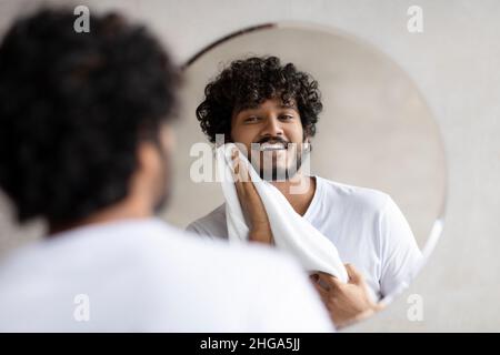 Alltagskonzept. Aufgeregt indischen Mann wischte sein Gesicht mit einem Handtuch, während im Bad stehen, Blick in den Spiegel Stockfoto