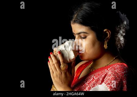 Eine schöne indische Frau in rot Saree weht Muschel auf schwarzem Hintergrund Stockfoto