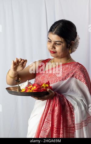 Eine wunderschöne indische Frau in rotem Saree, die Puja thali oder eine Gebetstafel auf weißem Hintergrund hält Stockfoto