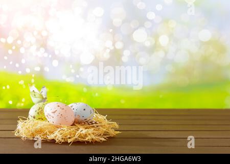 Ostereier, die in gedämpften Farben auf einem Heuernest vor einem frühlingshaften Gartenhintergrund gemalt sind, kopieren Platz für Happy Easter Text. Stockfoto