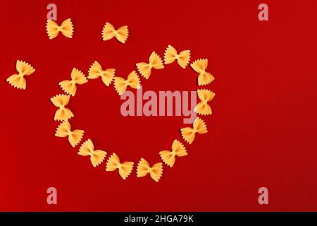 Hintergrund zum Valentinstag. Essen Valentinstag. Pasta-Farfalle-Bögen in Herzform auf rotem Hintergrund zum Valentinstag. Stockfoto