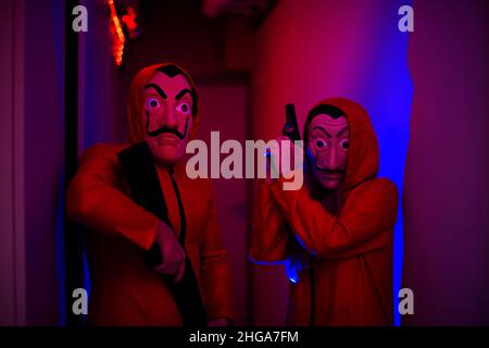 Polen, Krakau 28.08.2021 Menschen mit Waffen und Kostümen aus der Serie Money Heist / la casa de Papel in Masken von El Salvador wurden in Neon gegeben. Stockfoto