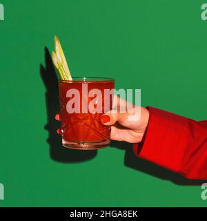 Weibliche Hand hält Glas mit Cocktail Bloody mary isoliert auf hellgrünen Neon-Hintergrund. Konzept des Geschmacks, alkoholische Getränke Stockfoto