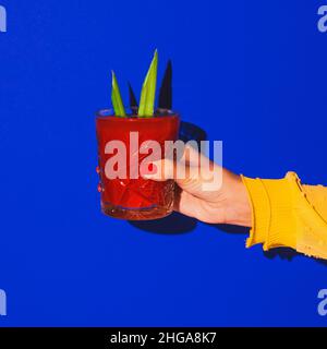 Weibliche Hand hält Glas mit Cocktail isoliert auf hellblauem Neon-Hintergrund. Konzept des Geschmacks, alkoholische Getränke Stockfoto