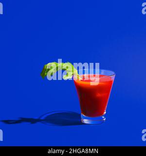 Kleines Glas mit Cocktail Bloody mary isoliert auf hellblauem Neon-Hintergrund. Konzept des Geschmacks, alkoholische Getränke Stockfoto