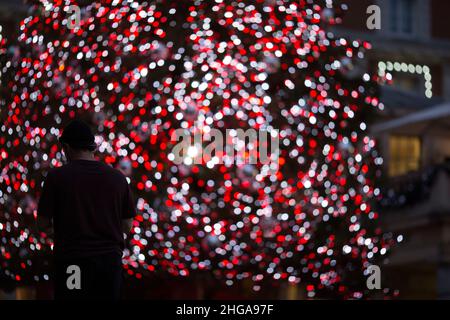 In Covent Garden, im Zentrum von London, wird am Nachrichtenabend eine Person vor festlichen Lichtern geschilhoutet. Stockfoto