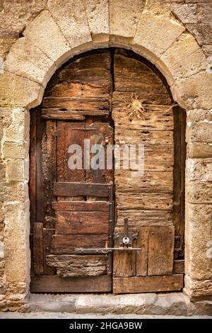 Sehr alte gewölbte Holztür mit kunstvollen Steinbogenbolzen und einem Vorhängeschloss Besula Spanien umgeben Stockfoto