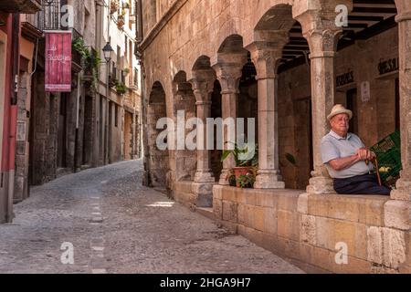 Ein alter Mann mit Strohhut und Spazierstock, der unter den Bögen in einer alten spanischen Straße Besalu Spanien ein Nickerchen macht Stockfoto