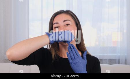Die Ärztin Kosmetologin gibt sich eine Gesichtsmassage im bukkalen Bereich, unterrichtet und zeigt eine orale neuromuskuläre Intra-Massage. Stockfoto