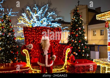 Warschau, Polen - 19. Dezember 2019: Hinter dem Rücken eines jungen Paares, das in der Weihnachtsmarkt-Szene Warszawa nachts mit dem Weihnachtsmann steht, beleuchtet Stockfoto