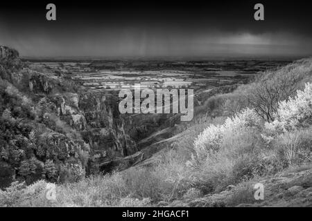 Eine Infrarotaufnahme der Cheddar Gorge in den Mendip Hills mit dem Dorf Cheddar und Somerset Levels im Hintergrund, Somerset, England. Stockfoto