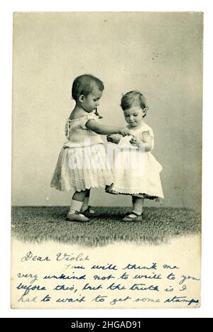 Edwardianische Grußkarte mit zwei niedlichen Kindern / Kleinkindern, die Hände halten, das Baby auf der linken Seite ist wahrscheinlich ein Junge, der ein Kleid trägt, wie es zu dieser Zeit normal war, geschrieben 1904 aus Großbritannien Stockfoto