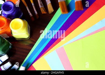 Kunst- und Handwerksausrüstungen, Kunstwerke, Farbpapier, Farbtuben und Pinsel auf einem Tisch, Studentenarbeit Stockfoto