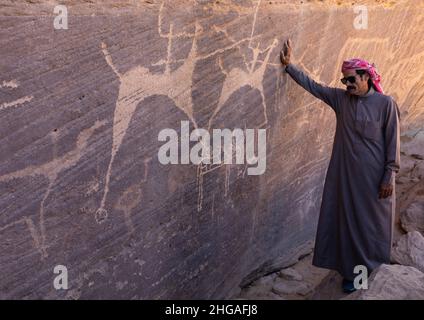 Saudi-Mann vor Felszeichnungen auf einem Felsen, auf dem Jäger auf Pferden reiten, Provinz Najran, Thar, Saudi-Arabien Stockfoto