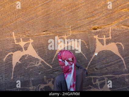 Saudi-Mann vor Felszeichnungen auf einem Felsen, auf dem Jäger auf Pferden reiten, Provinz Najran, Thar, Saudi-Arabien Stockfoto