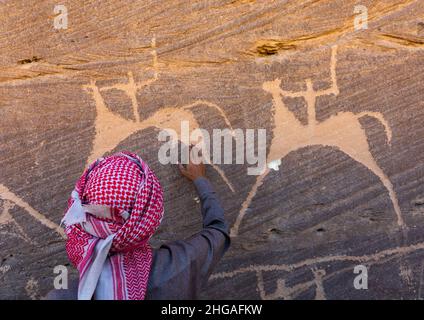 Saudi-Mann vor Felszeichnungen auf einem Felsen, auf dem Jäger auf Pferden reiten, Provinz Najran, Thar, Saudi-Arabien Stockfoto