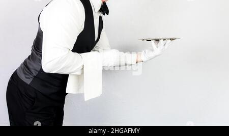 Profil Porträt von Butler oder Kellner in schwarzer Weste und weißen Handschuhen mit silbernem Serviertablett. Dienstleistungsbranche und Gastgewerbe. Stockfoto