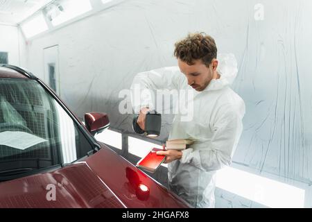 Der Automaler Mensch bestimmt den richtigen Ton einer Fahrzeugkarosserie mit Hilfe einer speziellen Koloristelampe. Karosseriewerkstatt in der Garage Stockfoto