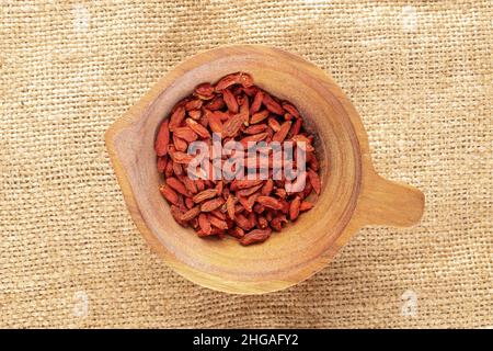 Getrocknete Bio-Goji-Beeren in einem Holzbecher auf einem Sackleinen, Makro, Draufsicht. Stockfoto