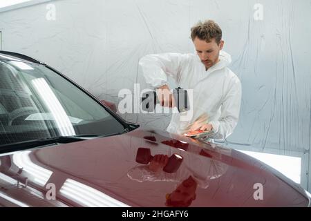 Der Automaler Mensch bestimmt den richtigen Ton einer Fahrzeugkarosserie mit Hilfe einer speziellen Koloristelampe. Karosseriewerkstatt in der Garage Stockfoto