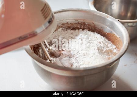 Herstellung eines Schokoladenkuchens: Hinzufügen von trockenen Zutaten. Rührbesen in Bewegung mit Bewegungsunschärfe. Stockfoto