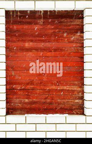 Fenster in Steinwand mit Holzbrettern im Winter bedeckt, schneit es. Als illustrativen Hintergrund. Stockfoto