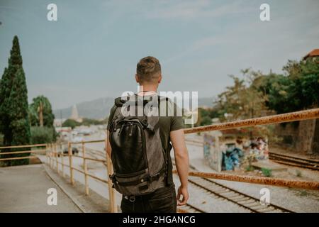 Ein Tourist mit Rucksack reist alleine. Ein Mann wartet auf seinen Zug und genießt einen Blick auf die Berge. Stockfoto