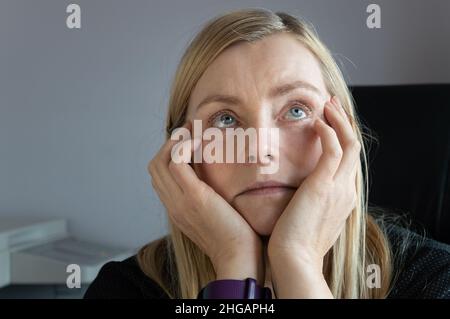 Gelangweilte Frau, die im Büro sitzt und in die Decke schaut Stockfoto