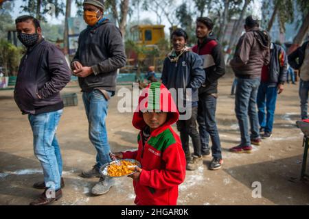 Ghaziabad, Indien. 19th Januar 2022. Ein junger Junge schaut zu, während er einen Teller Nahrung in einem subventionierten Nahrungsmittelzentrum in Vashundhara hält.Ein Nahrungsmittelzentrum, das von Tirthankar Mahavir Manav Seva Trust (einem gemeinnützigen Treuhandwerk für soziale Zwecke in Indien) betrieben wird, berechnen sie 5 indische Rupien für pro Teller Nahrung, Die meisten Nutznießer aus dem ärmsten Teil der Gesellschaft, die stark von der Pandemie und der Sperrung betroffen waren, kommen immer und nehmen ihr Nahrung. Kredit: SOPA Images Limited/Alamy Live Nachrichten Stockfoto