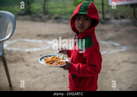 Ghaziabad, Indien. 19th Januar 2022. Ein junger Junge schaut zu, während er einen Teller Nahrung in einem subventionierten Nahrungsmittelzentrum in Vashundhara hält.Ein Nahrungsmittelzentrum, das von Tirthankar Mahavir Manav Seva Trust (einem gemeinnützigen Treuhandwerk für soziale Zwecke in Indien) betrieben wird, berechnen sie 5 indische Rupien für pro Teller Nahrung, Die meisten Nutznießer aus dem ärmsten Teil der Gesellschaft, die stark von der Pandemie und der Sperrung betroffen waren, kommen immer und nehmen ihr Nahrung. Kredit: SOPA Images Limited/Alamy Live Nachrichten Stockfoto