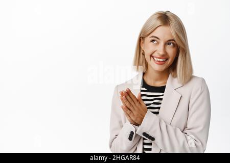 Lächelnd erfolgreicher makler, Verkäuferin, die sich die Hände reibt, klatscht und ein süffes Gesicht macht, das Ziel erreicht, das Einkommen genießt und über Weiß steht Stockfoto