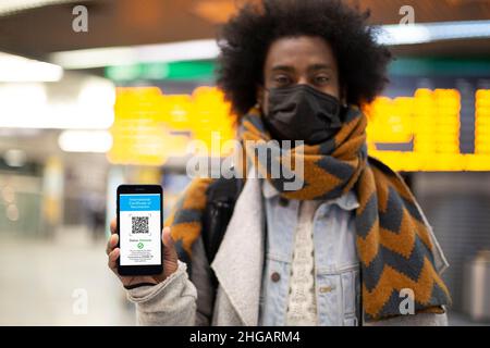 Junger afroamerikanischer Mann, der seinen digitalen Impfpass am Flughafen vorzeigt. Selektiver Fokus. Covid-Pass für Reisen. Stockfoto