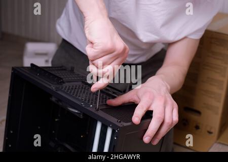 Ein Mann zu Hause sammelt, zerlegt einen Computer. Hände eines Mannes halten Drähte, verbindet Drähte. Sammeln eines Computers für Profis, ein Gaming-Computer Stockfoto