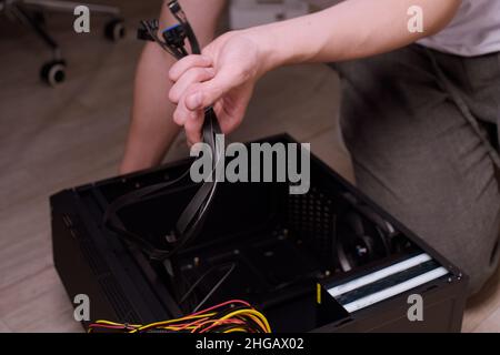 Ein Mann zu Hause sammelt, zerlegt einen Computer. Hände eines Mannes halten Drähte, verbindet Drähte. Sammeln eines Computers für Profis, ein Gaming-Computer Stockfoto