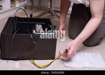 Ein Mann zu Hause sammelt, zerlegt einen Computer. Hände eines Mannes halten Drähte, verbindet Drähte. Sammeln eines Computers für Profis, ein Gaming-Computer Stockfoto