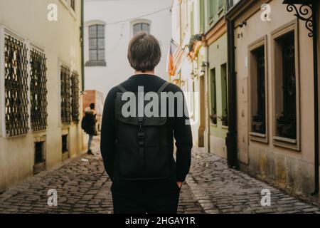 Ein Mann reist in Europa auf der Straße durch die Straßen der Altstadt, mit einer Aktentasche. Student reist allein. Ein junger Mann Stockfoto