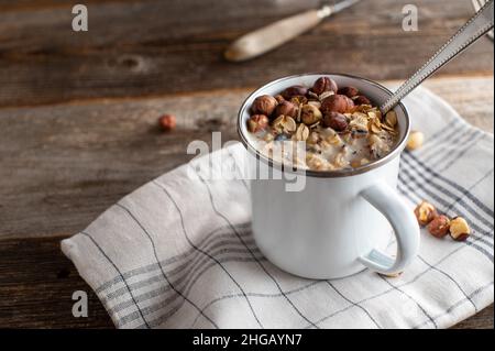 Haferbrei mit gerösteten Haselnüssen in einer weißen Emaille-Tasse mit Löffel Stockfoto