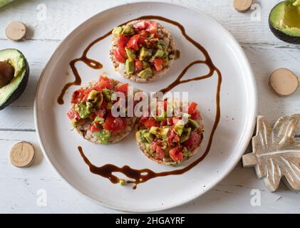 Salat mit gehackten Avocados und Tomaten, mariniert mit einem Balsamico-Dressing, serviert als Sandwich auf braunem Reiskracker auf weißem Hintergrund. Stockfoto