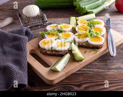 Gekochtes Ei-Sandwich mit Vollkornbrot, Butter und Schnittlauch auf einem Holztisch. Stockfoto