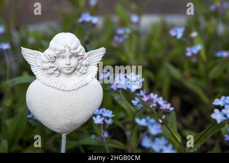 Weiße Engelsfigur mit Herz in einem Blumenbeet Stockfoto