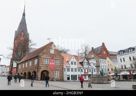 Flensburg, Deutschland - 9. Februar 2017: Nordermarkt, Stadtplatz mit Neptunbrunnen und Marienkirche. Gewöhnliche Menschen gehen die Straße entlang Stockfoto