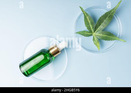 Glasflasche mit cbd-Öl auf blauem Hintergrund mit Marihuana-Blatt. Kosmetika auf Hanfbasis. Natürliches ätherisches Pflanzenhanf-Öl in einer Pipettenflasche aus Glas. Stockfoto