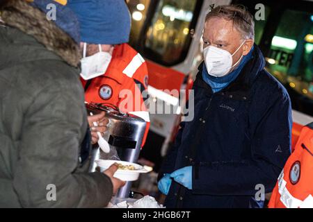 Hannover, Deutschland. 19th Januar 2022. Stephan weil (r, SPD), Ministerpräsident von Niedersachsen, verteilt gemeinsam mit den Helfern des Kältebusses der Johanniter-Unfall-Hilfe auf dem Goseriedeplatz Essen an bedürftige. Weil hat am Mittwochabend Essen und Getränke an Obdachlose in Hannover verteilt. Quelle: Moritz Frankenberg/dpa/Alamy Live News Stockfoto