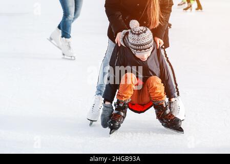 Weich, selektive Fokus.Mama mit Baby Junge 6 Jahre alt, lernen Zug, reiten Winterstadt Eislaufen. Das Kind steht auf, fällt auf Schlittschuhe, kniet, spielt Stockfoto