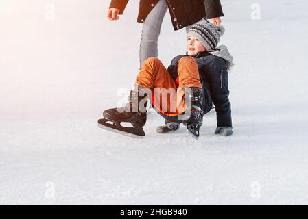 Weich, selektive Fokus.Mama mit Baby Junge 6 Jahre alt, lernen Zug, reiten Winterstadt Eislaufen. Das Kind steht auf, fällt auf Schlittschuhe, kniet, spielt Stockfoto