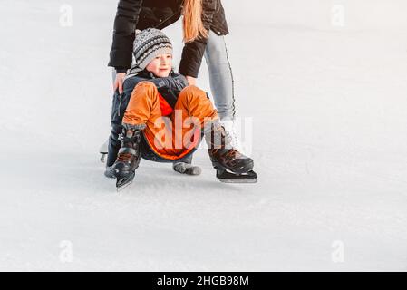 Weich, selektiver Fokus. Sport.Mom mit Baby Junge 6 Jahre alt, lernen Zug, Fahrt Winter City Eisbahn, Eislaufen. Das Kind steht auf, fällt auf Schlittschuhe, kniet Stockfoto