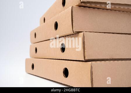 Stapeln Sie flache Pizzakartons aus braunem Karton auf weißem Hintergrund. Stockfoto