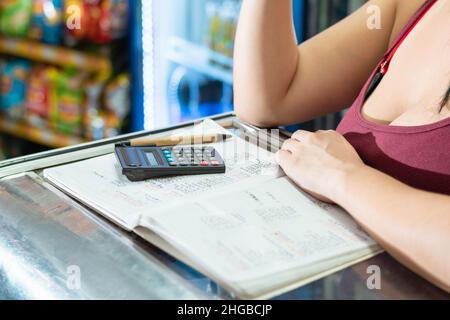 latina Frau mit den Händen auf der Vitrine. Mit ihrem kleinen Taschenrechner und dem umweltfreundlichen Pappstift auf einem großen Notizbuch. Berechnungen durchführen Stockfoto