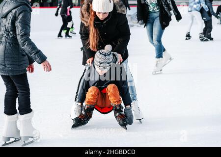 Weich, selektive Fokus.Mama mit Baby Junge 6 Jahre alt, lernen Zug, reiten Winterstadt Eislaufen. Das Kind steht auf, fällt auf Schlittschuhe, kniet, spielt Stockfoto